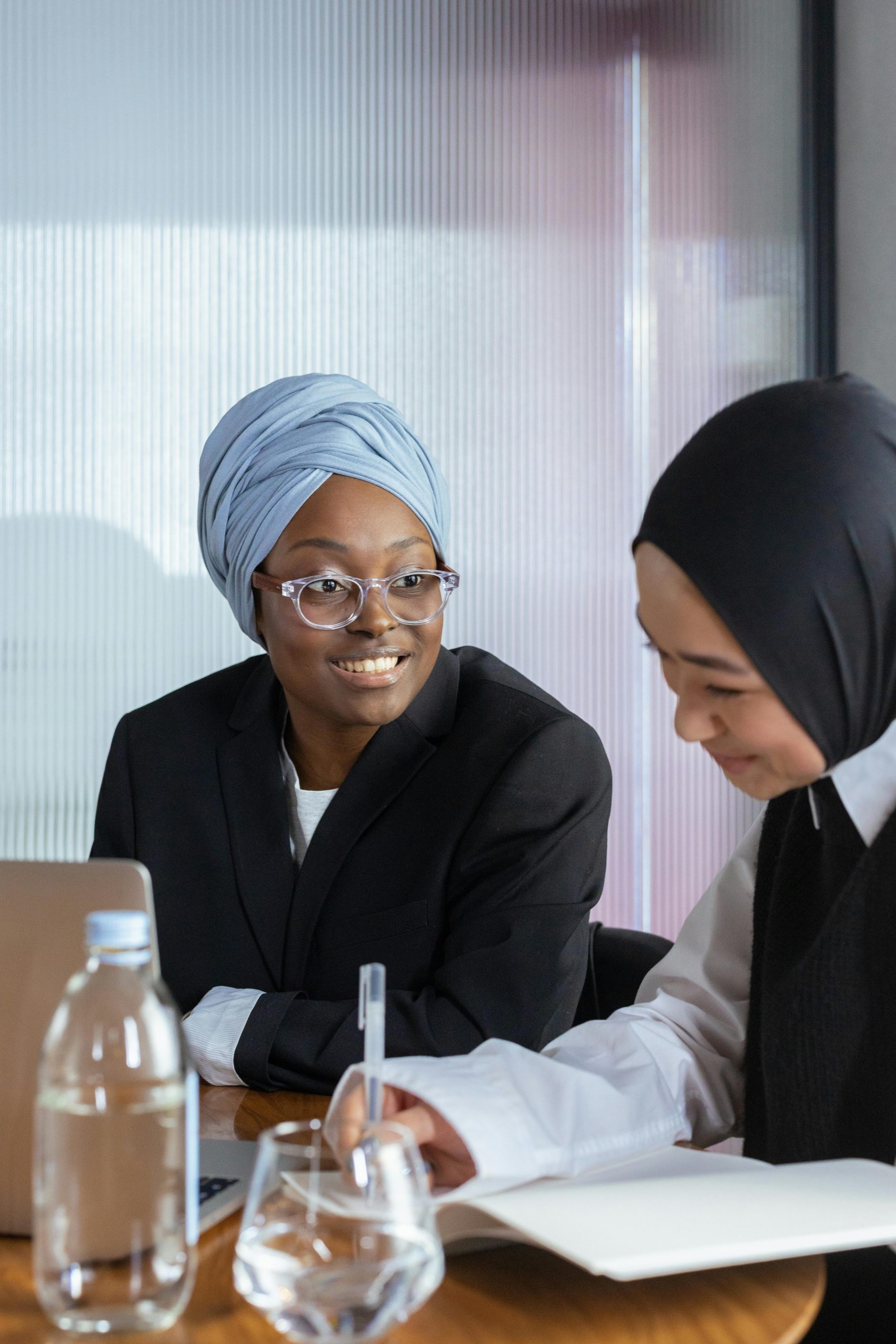 Two diverse businesswomen in hijabs collaborating at a modern office desk.